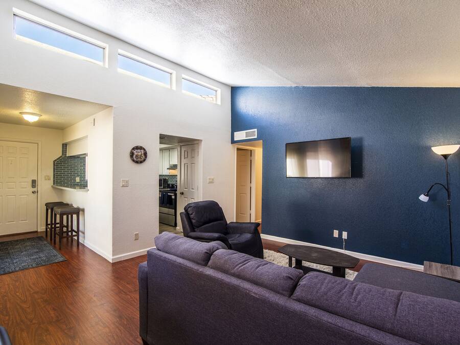 A living room with a dark blue accent wall, a flat-screen TV mounted above a wooden coffee table, and a large gray sectional sofa.