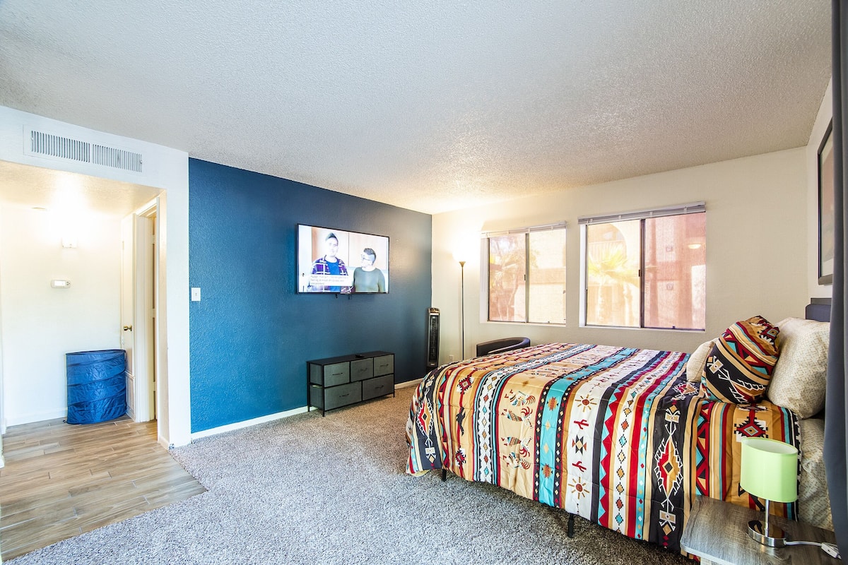 A bedroom with a large bed, a TV on the wall, and a window.
