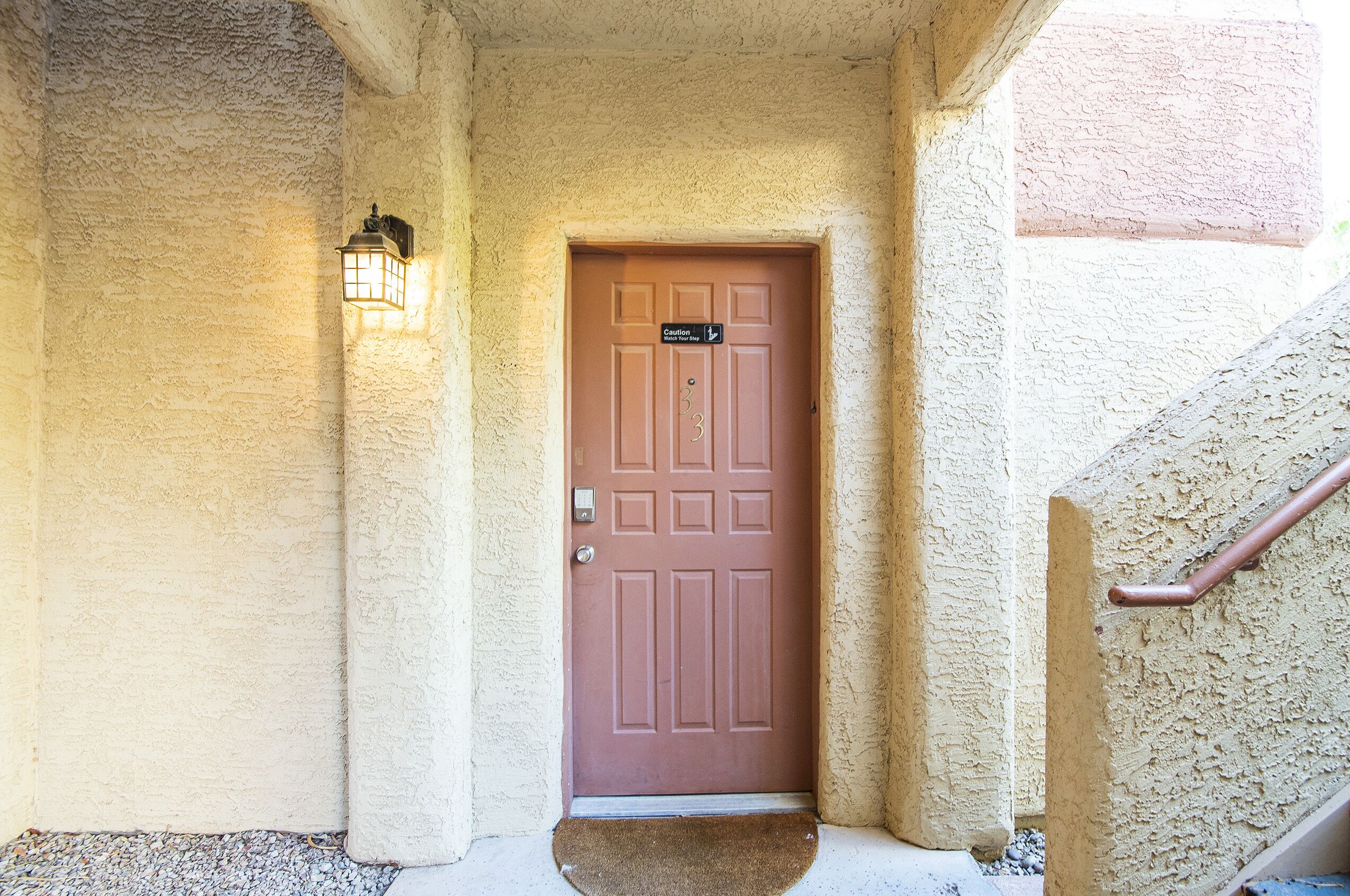 A brown door with a caution sign, a textured wall, and a small step leading to a landing.