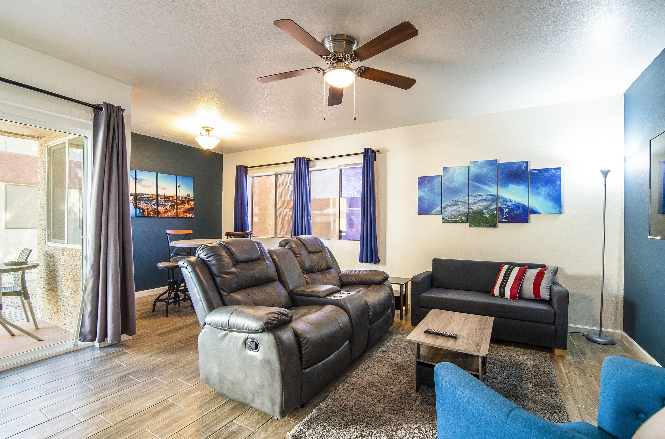 A living room with a reclining sofa, a coffee table, a blue armchair, and a ceiling fan.
