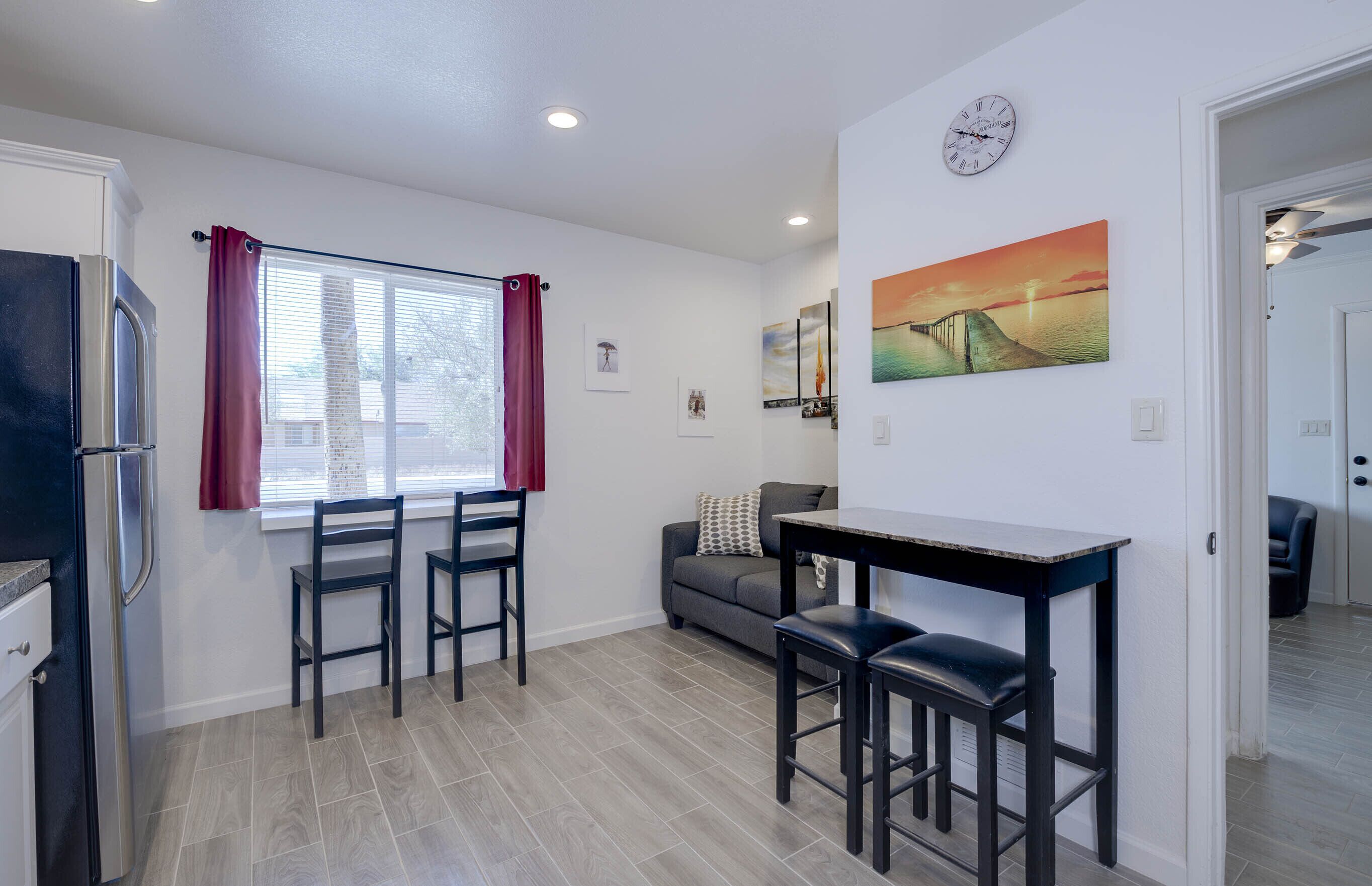 A modern kitchen with a dining area, featuring a refrigerator, two chairs, a table, and a sofa.