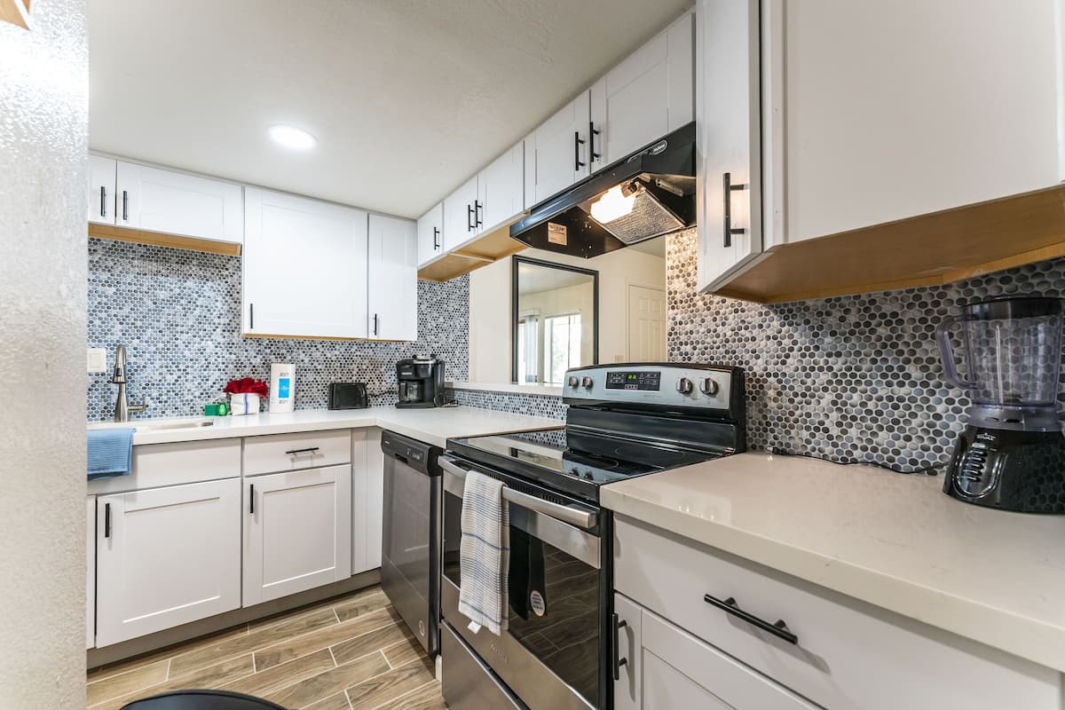 A modern kitchen with white cabinets, a stainless steel oven, a coffee maker, and a blender on the counter.
