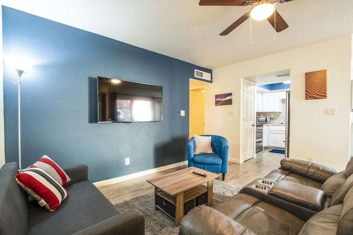 A living room with a blue wall, a ceiling fan, a flat-screen TV, a sofa, a coffee table, and a blue armchair.