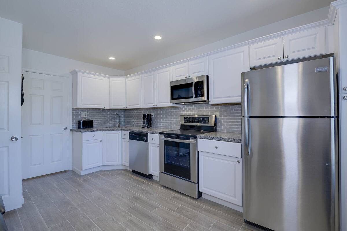 A modern kitchen with white cabinets, stainless steel appliances, and a tiled backsplash.