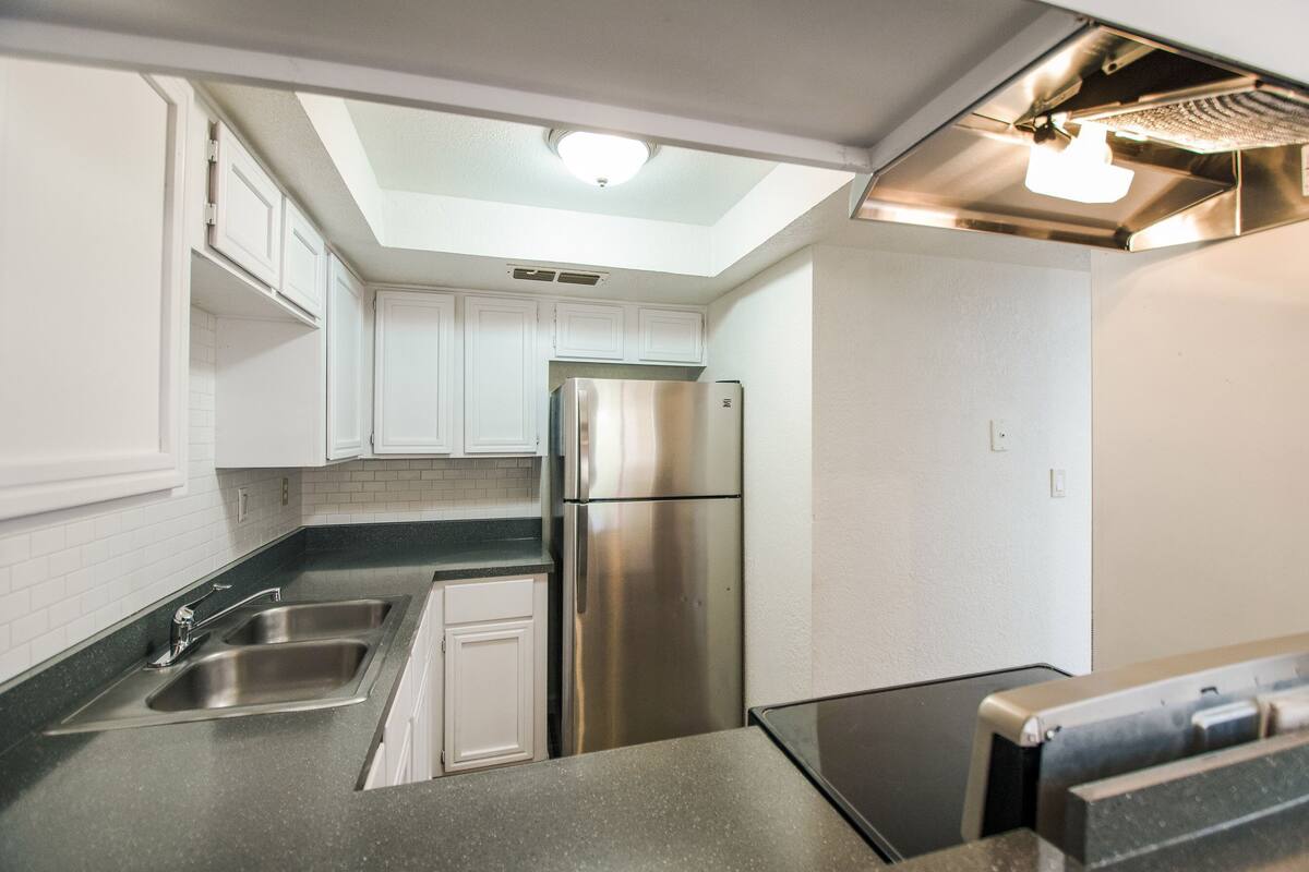 A compact kitchen with white cabinets, stainless steel appliances, and a skylight.