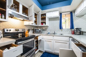 Een moderne keuken met witte kastjes, een roestvrijstalen fornuis, een magnetron en een raam met blauwe gordijnen.
