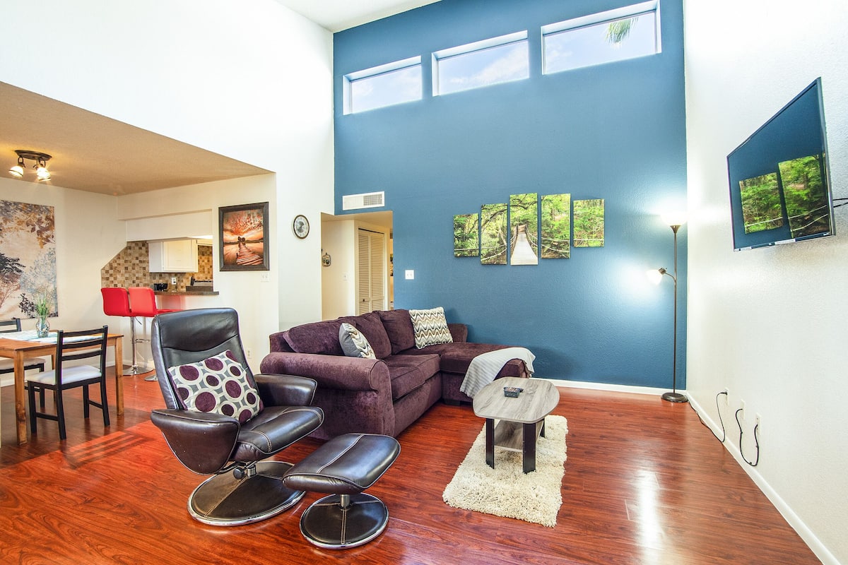 A living room with a sectional sofa, a leather chair, and a dining area with a table and chairs.