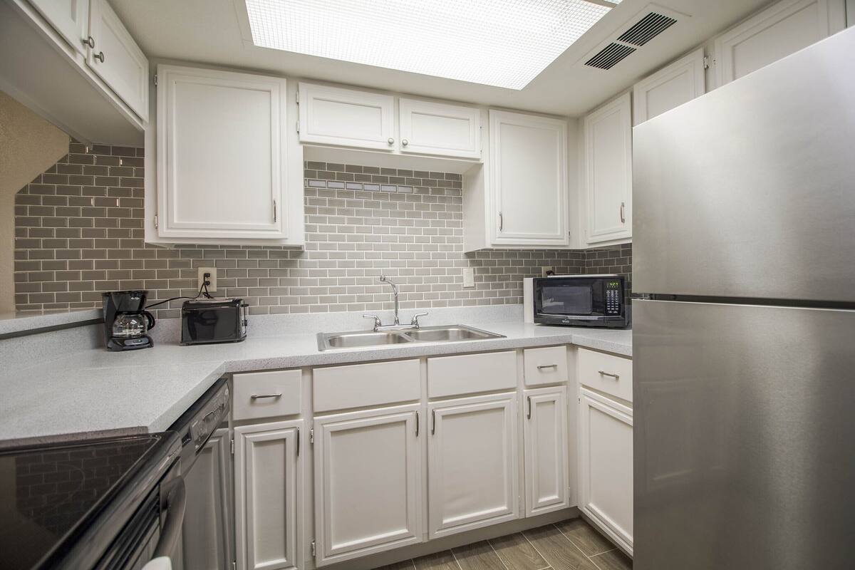 A kitchen with white cabinets, a stainless steel refrigerator, a microwave, and a coffee maker.