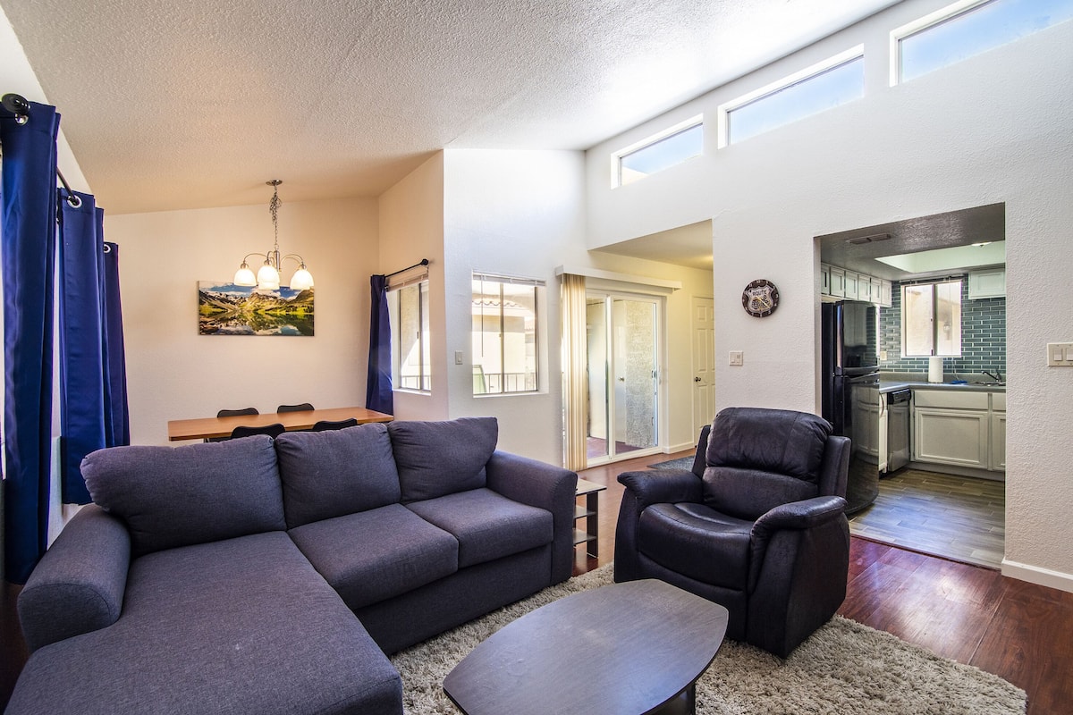 A modern living room with a sectional sofa, a recliner, and a dining area with a table and chairs.