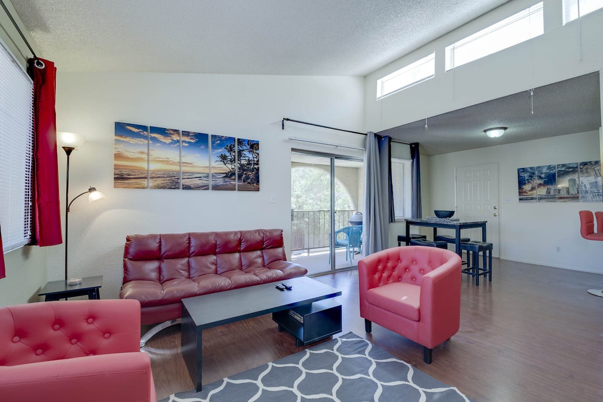 A modern living room with a leather sofa, a coffee table, and a pink armchair. There is a dining area with a table and chairs visible through a glass door.