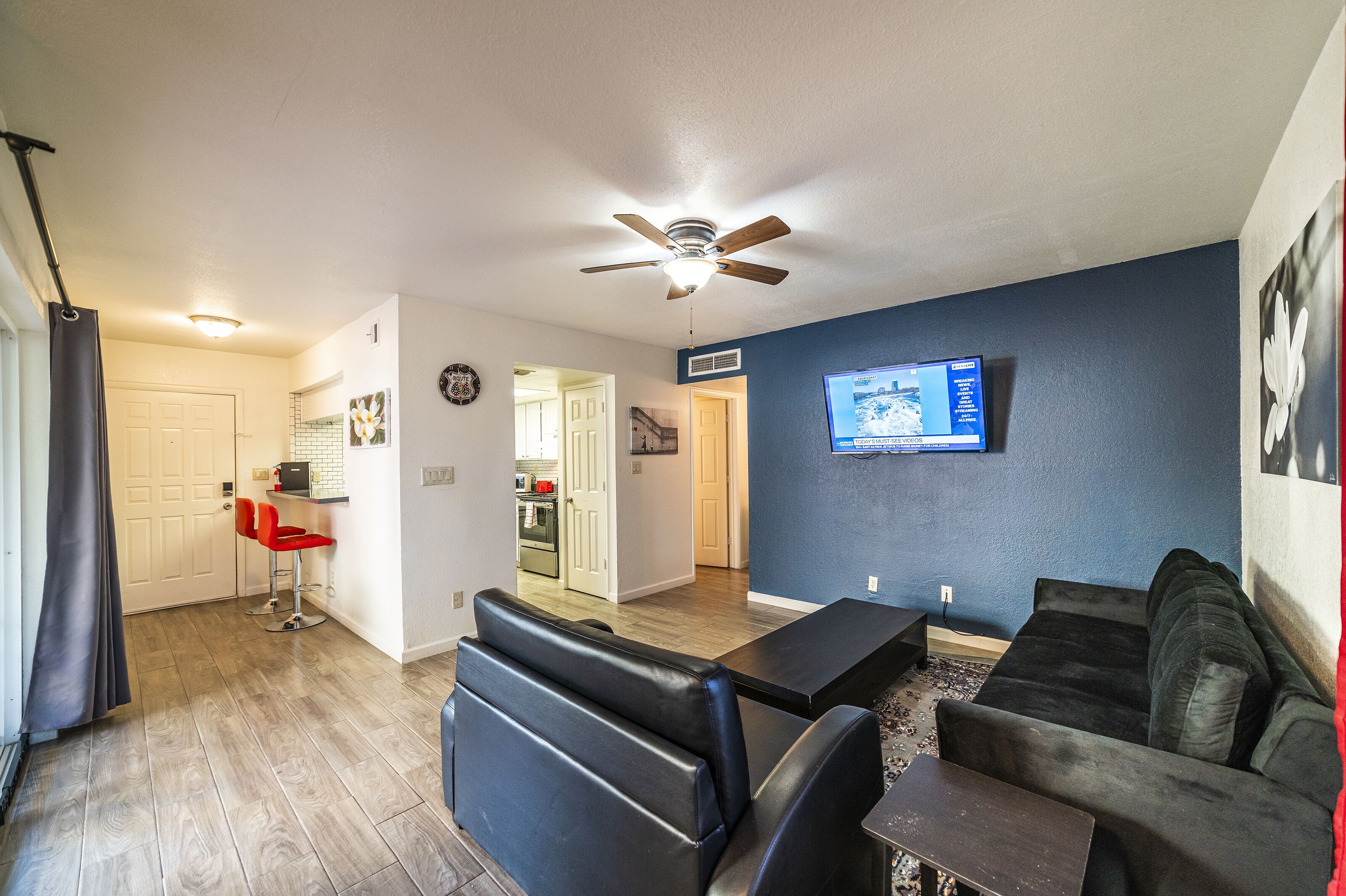 A modern living room with a ceiling fan, a TV mounted on the wall, and a dining area with a table and chairs.