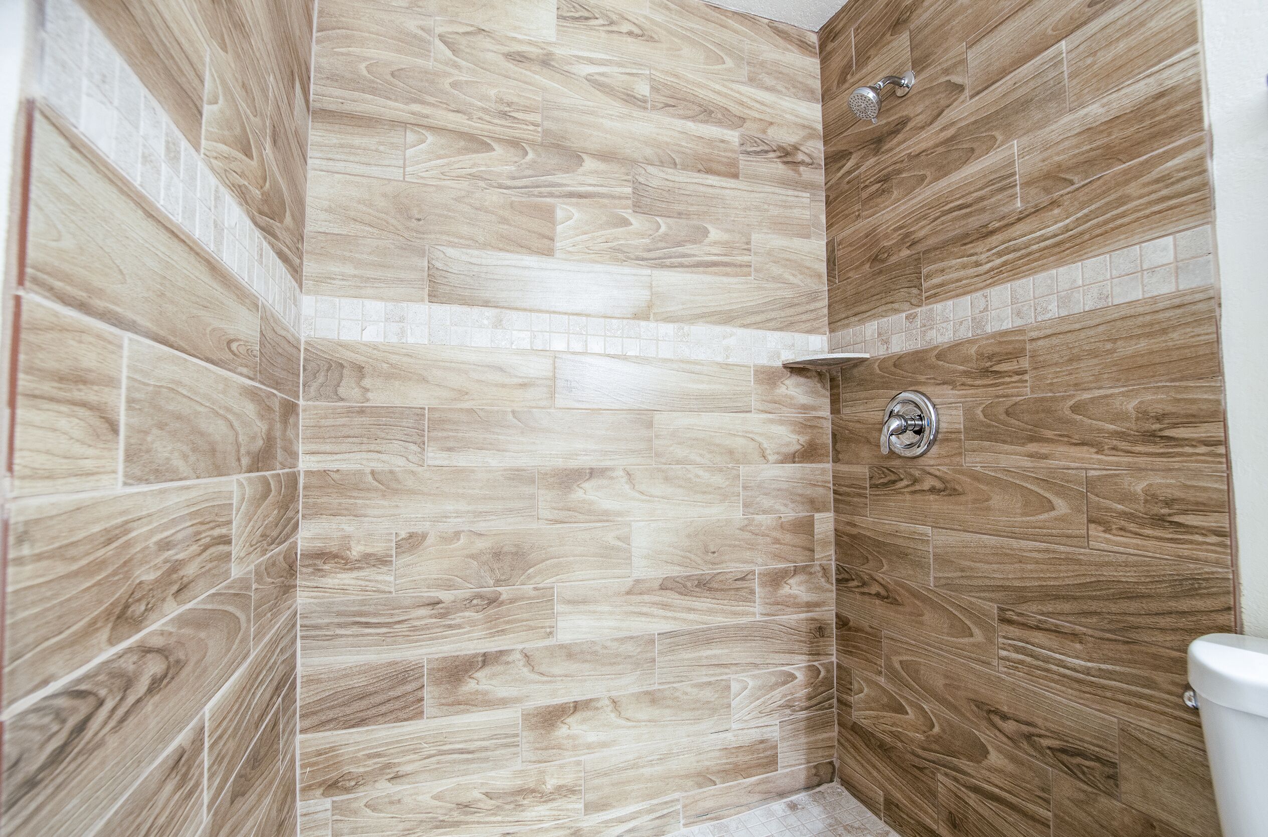A shower area with wooden wall tiles and a visible showerhead.