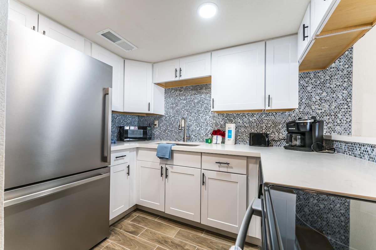 A modern kitchen with stainless steel appliances, white cabinetry, and a tiled backsplash.