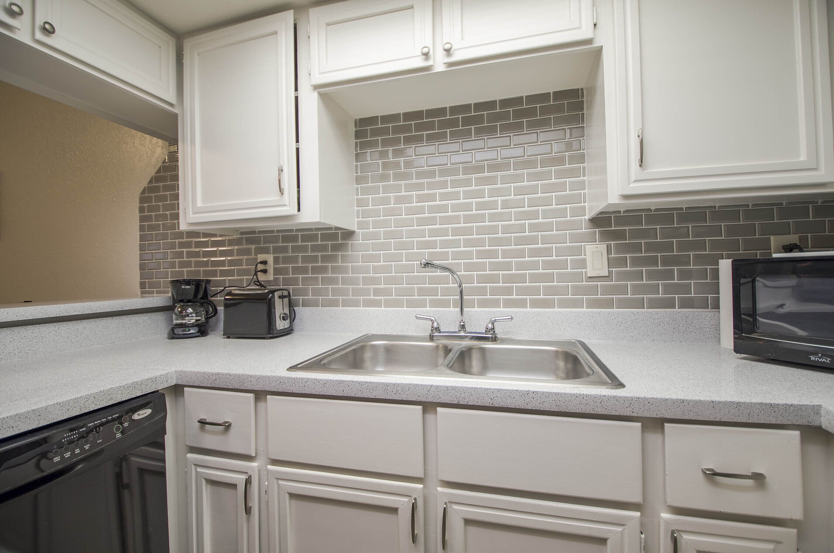 A kitchen with white cabinets, a double sink, a microwave, a coffee maker, and a dishwasher.