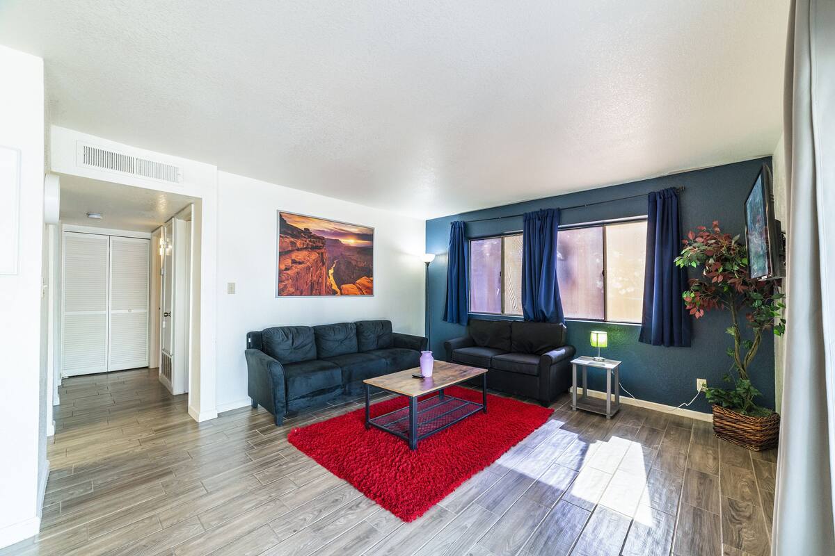 A living room with a red rug, two black sofas, a wooden coffee table, and a painting on the wall.