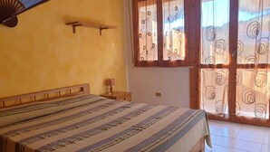 Ein Schlafzimmer mit einem Bett, einem Nachttisch, einem Wandventilator und einem Fenster mit Vorhängen.