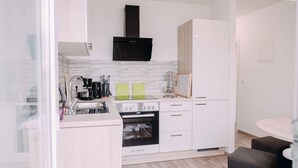 A compact kitchen with white cabinets, a black range hood, a built-in oven, and a small dining area with a round table and two stools.
