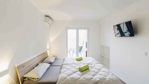 A small, bright room with two beds, a window, and a mounted TV.