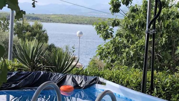 A pool with a view of a body of water, surrounded by greenery and a pergola structure.