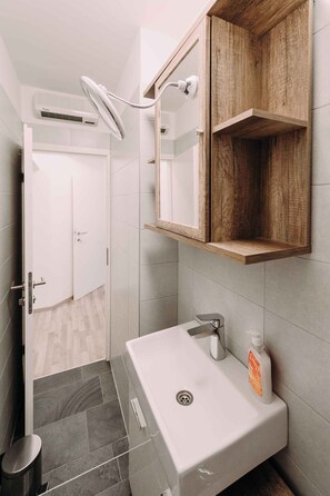 A bathroom with a white sink, a mirror, and a wooden shelf.