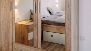 A wooden wardrobe with mirrored doors, a bed with white bedding, and a bedside table with a lamp. - Holiday apartment Sara with sea views and pool (Klimno)