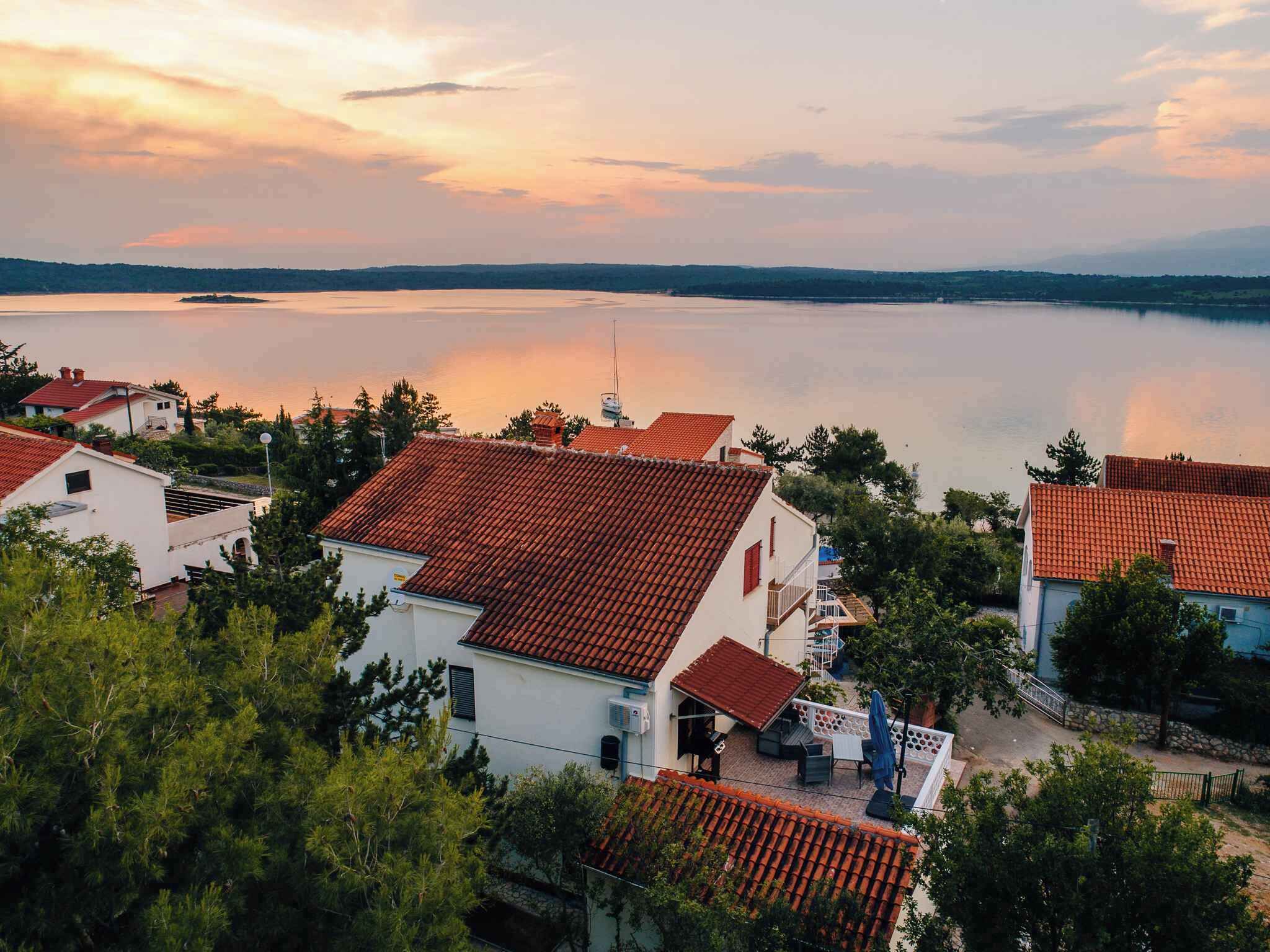 A coastal village with terracotta-roofed houses, a calm lake, and a clear sky.