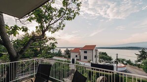 A balcony with chairs and a table, overlooking a lake and buildings with red roofs. - Holiday apartment Sara with sea views and pool (Klimno)