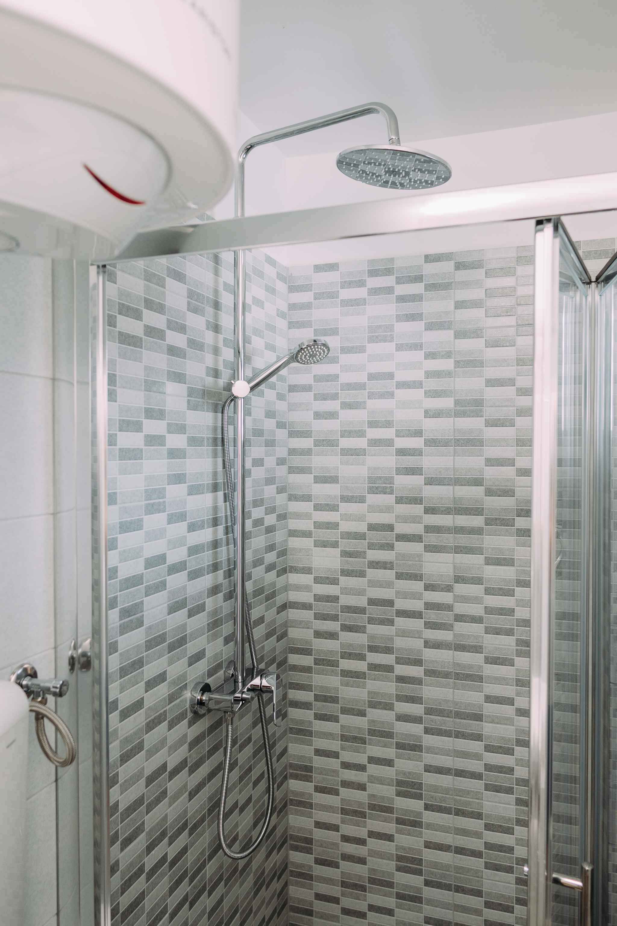 A glass-enclosed shower with a checkered tile wall, a handheld showerhead, and a wall-mounted faucet.