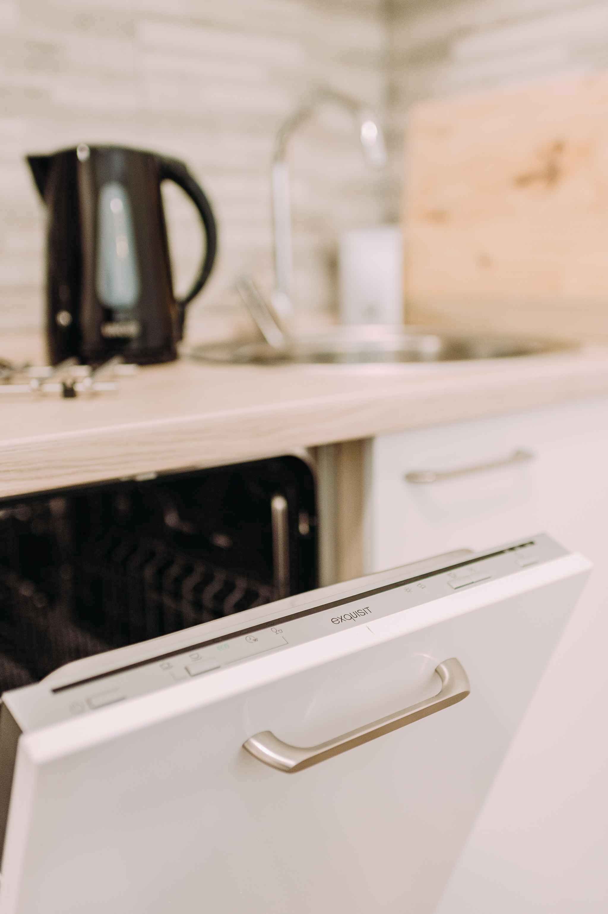 Una cocina con un lavavajillas blanco, una cafetera negra y una tabla de cortar de madera.