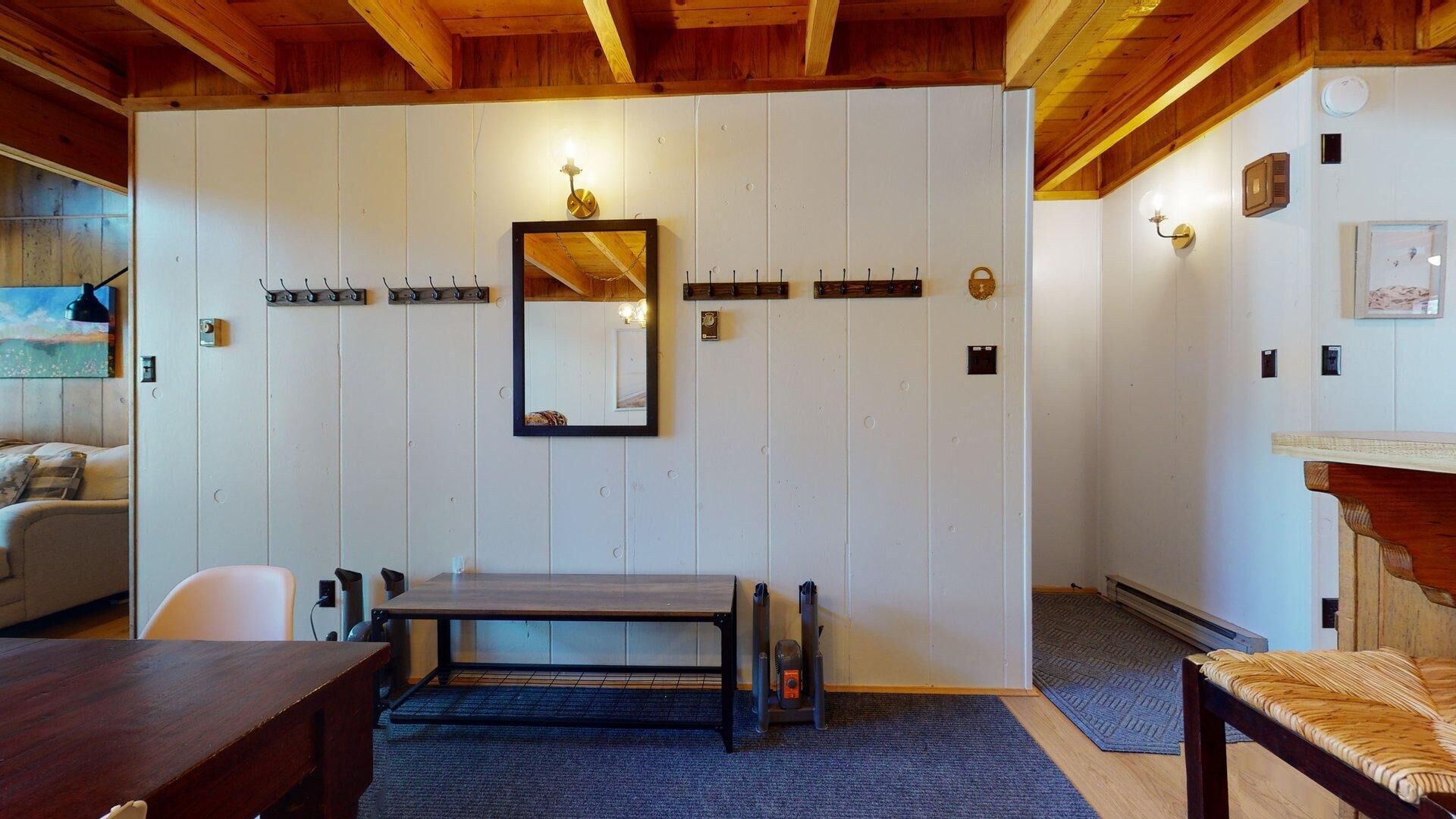 Ein Zimmer mit Holzboden, einem großen Spiegel, einem Tisch, Stühlen, einem Heizgerät und einem kleinen Teppich.