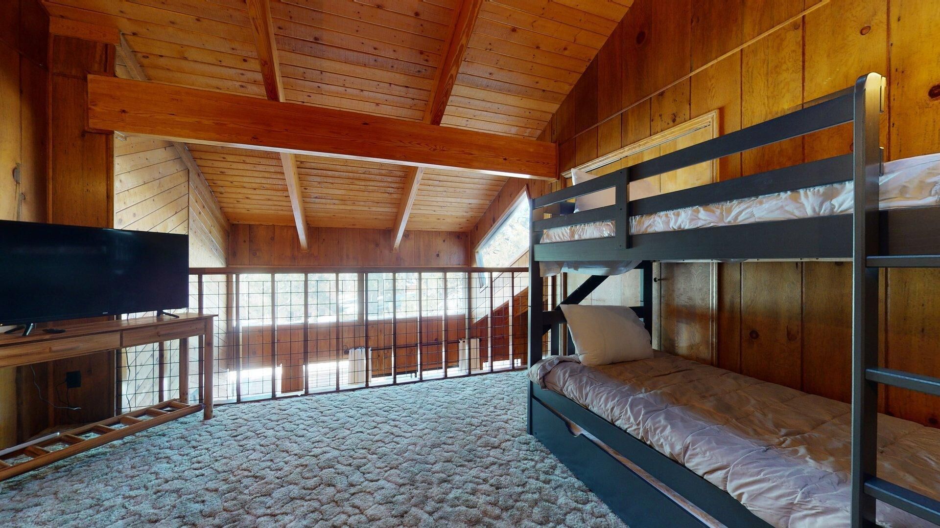 A wooden cabin room with bunk beds, a television, and a large window.