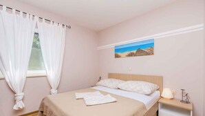 A bedroom with a bed, a nightstand, a painting, and a window with curtains.