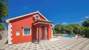 A red house with a tiled roof, a swimming pool, and a paved patio area.