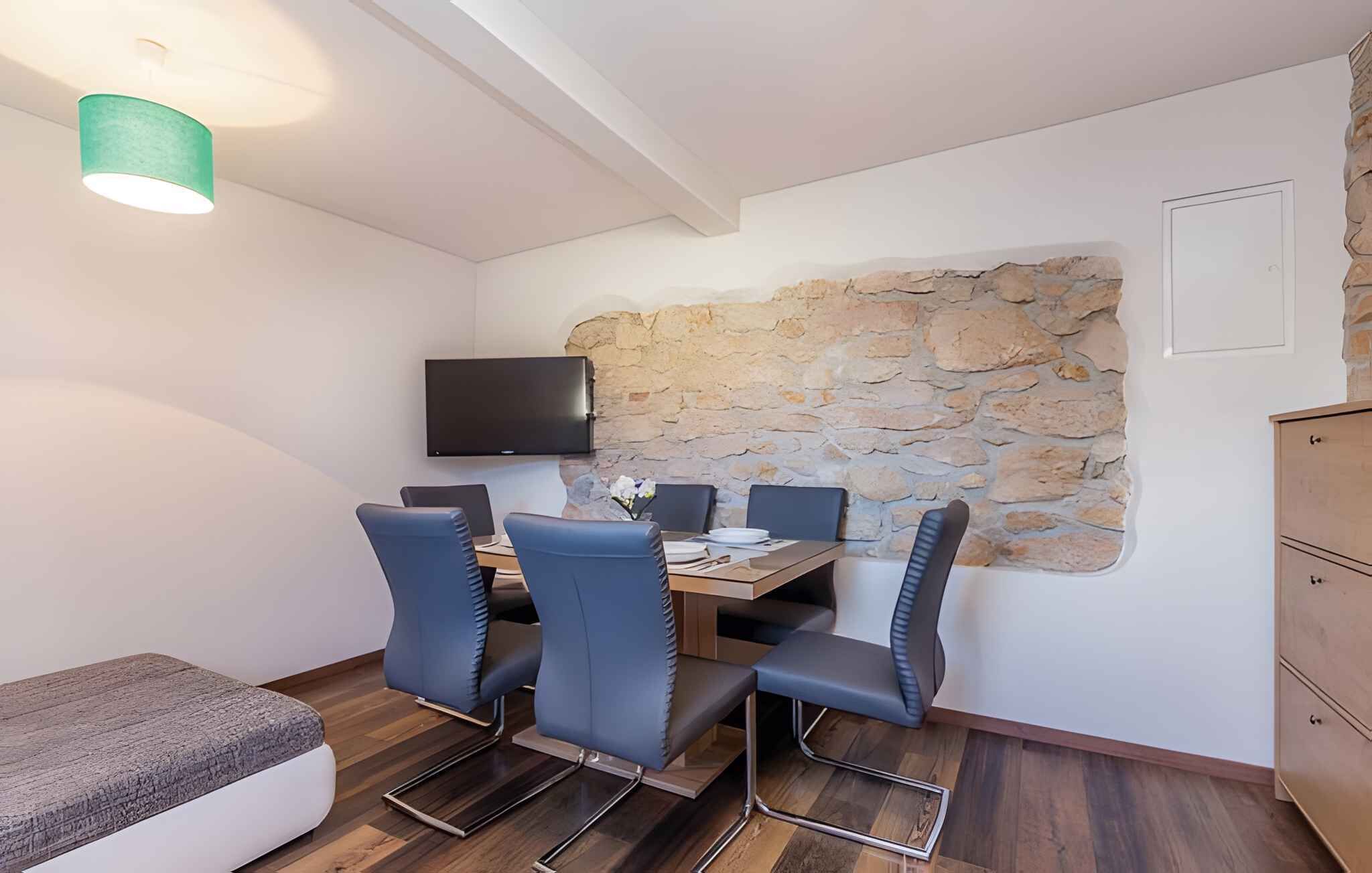 A dining area with a stone wall, a flat-screen TV mounted above a wooden table, and blue chairs.