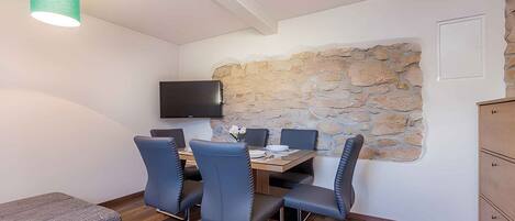 A dining area with a stone wall, a flat-screen TV mounted above a wooden table, and blue chairs.
