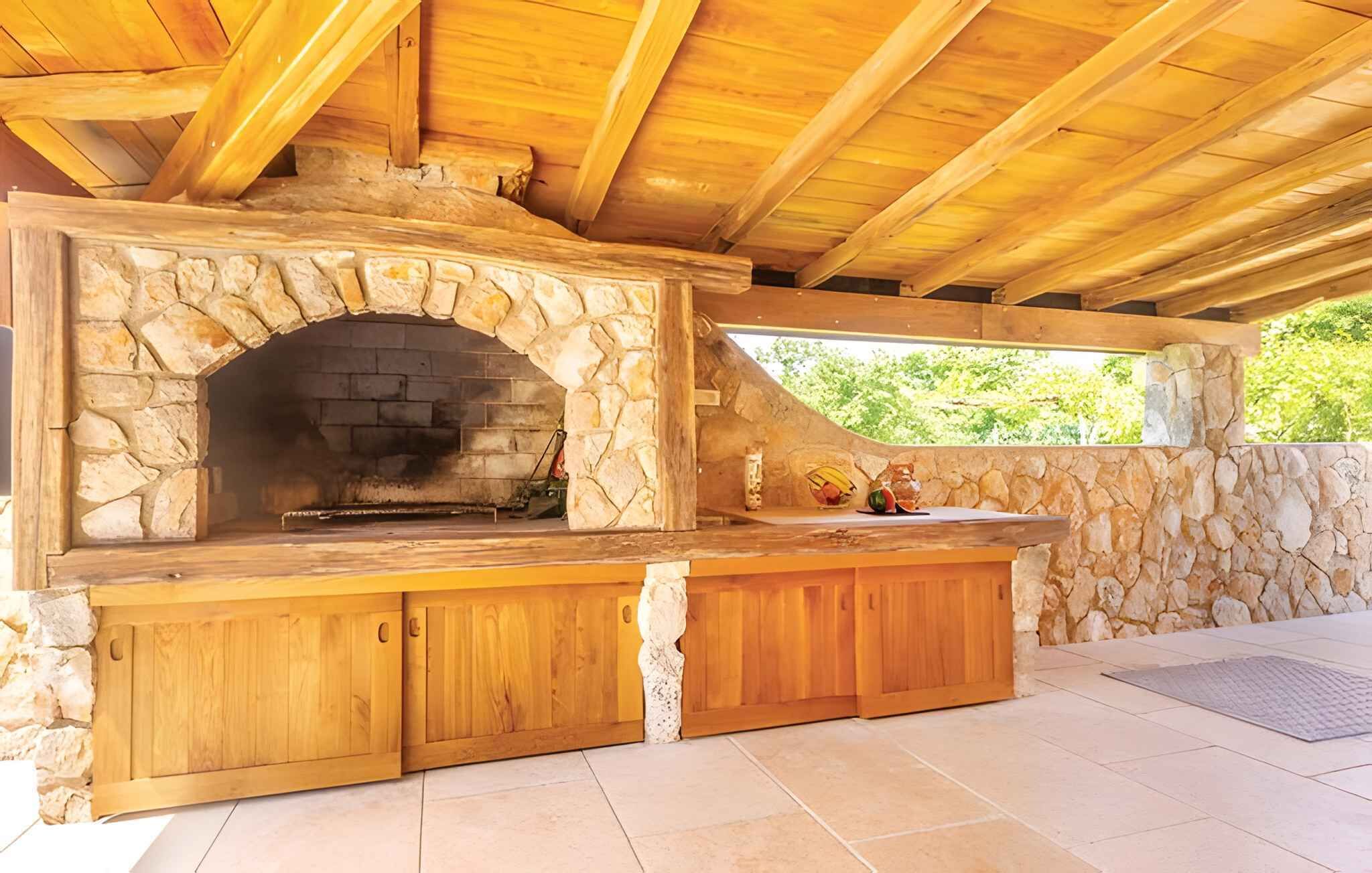 An outdoor stone oven with a wooden counter and cabinets, under a wooden roof structure.