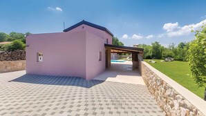 Uma casa moderna com fachada rosa, um muro de arrimo de pedra e área de piscina.