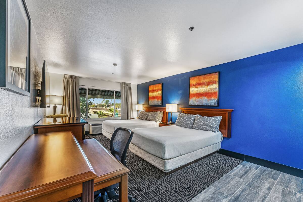 A hotel room with two beds, a desk, a chair, and artwork on the walls.