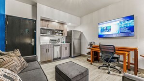 A modern kitchen with stainless steel appliances, a dining area with a wooden table and chairs, and a flat-screen TV mounted on the wall.
