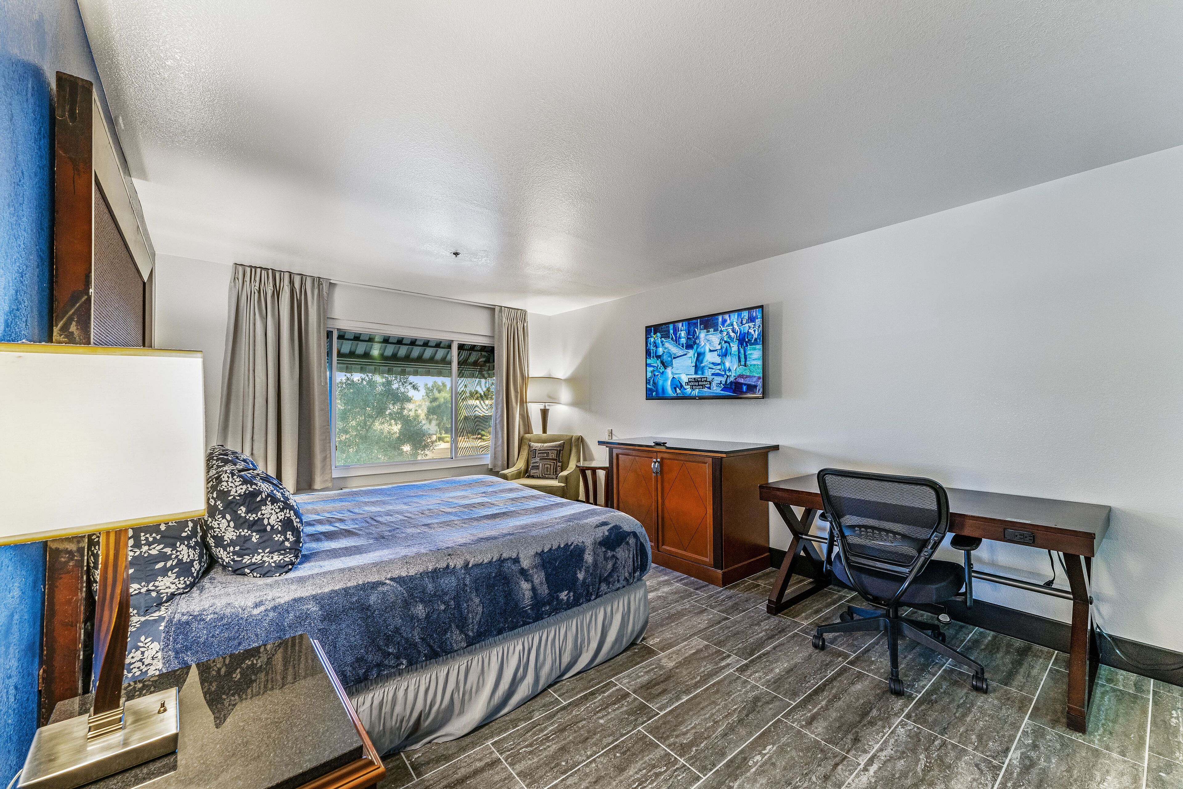 A hotel room with a bed, a desk, a chair, a TV, and a window with curtains.