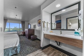 Habitación de hotel con cama, baño con un espejo grande, lavamanos y ventana con cortinas.