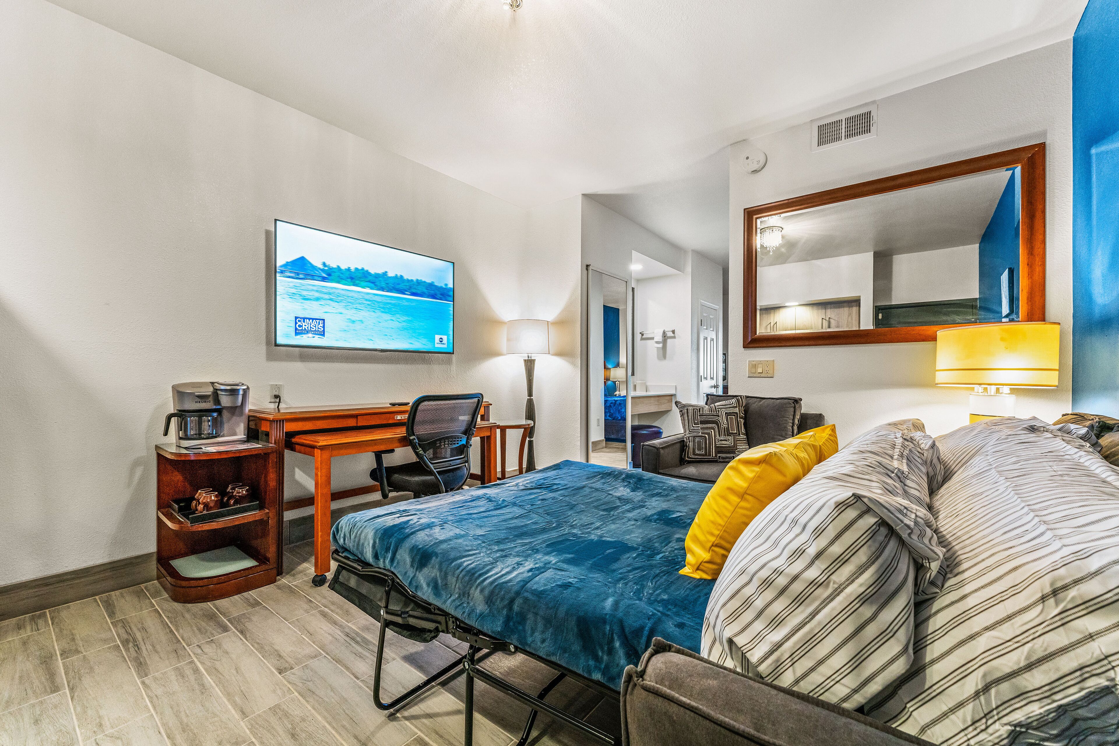 A hotel room with a bed, desk, chair, TV, and a mirror.
