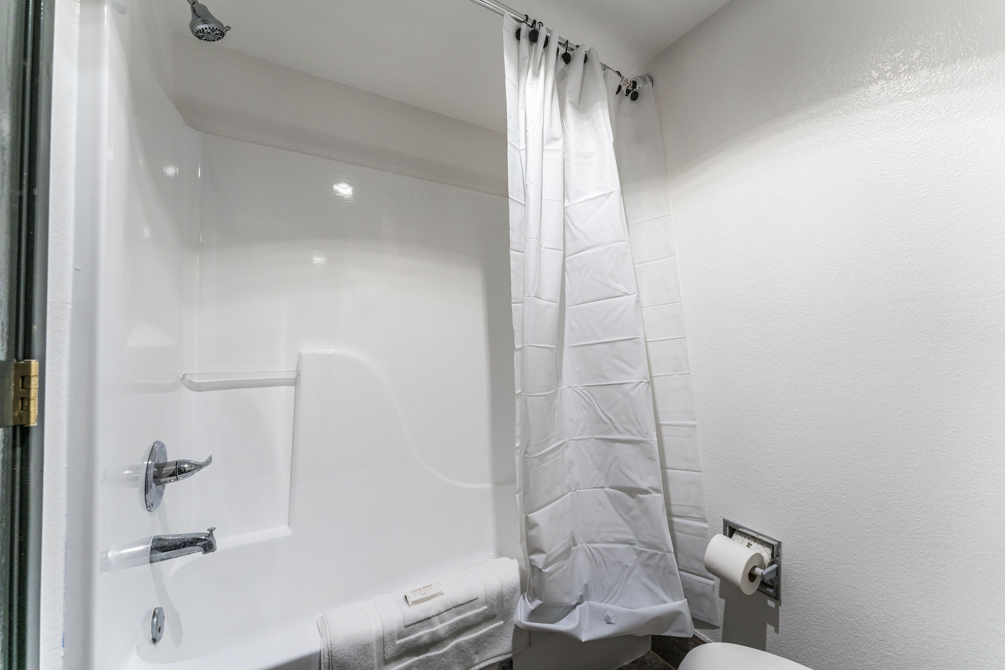 A bathroom with a white bathtub, a shower curtain, a toilet, and a towel rack.