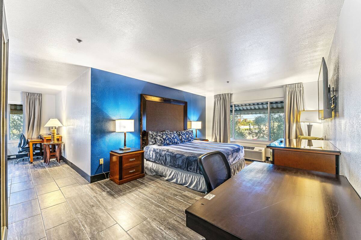 A modern hotel room with a large bed, bedside tables, a desk, and a view of the outdoors.