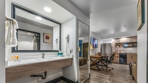 A modern bathroom with a large mirror, sink, and shower. It includes a vanity with a wooden countertop and a tiled floor.