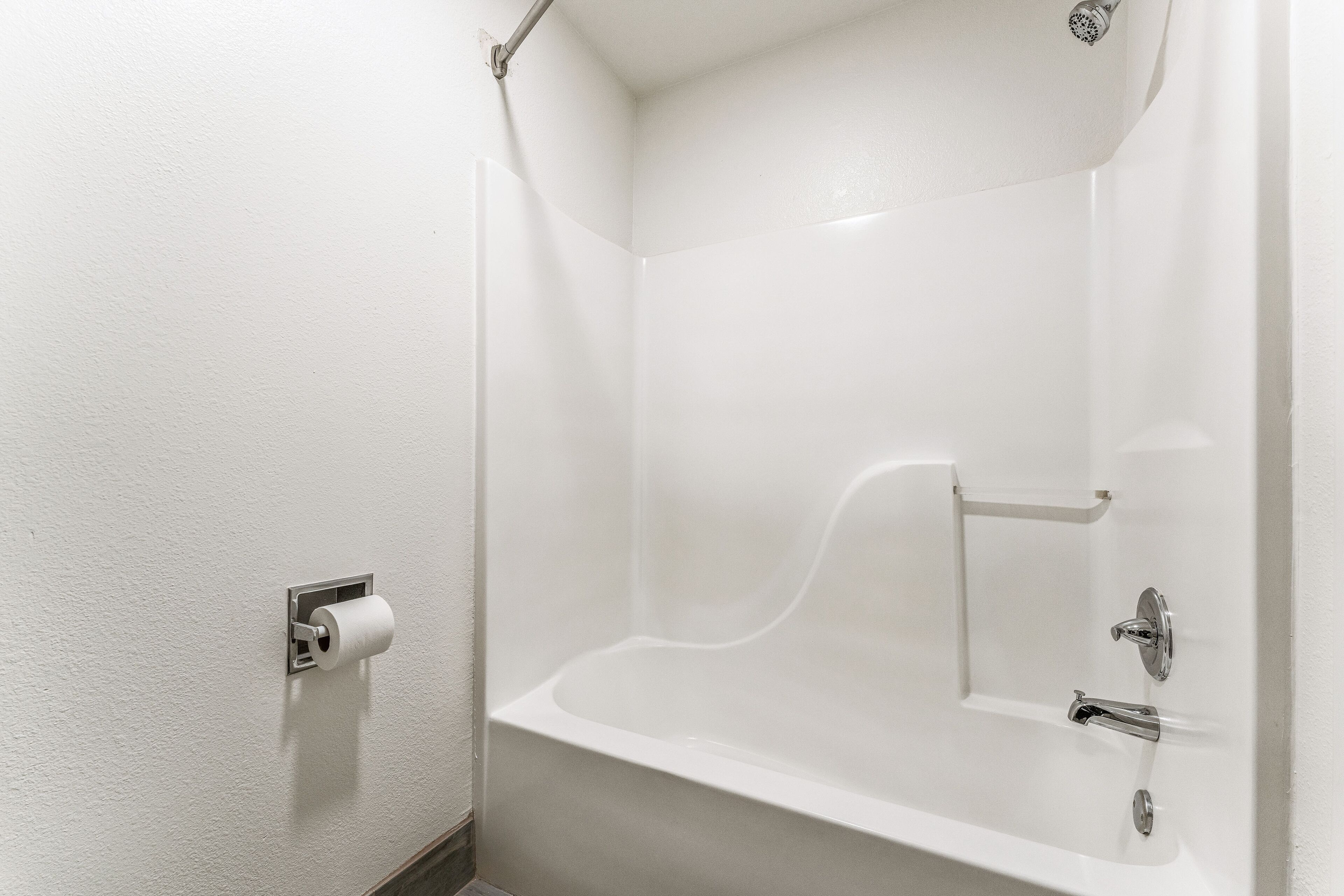 Un baño blanco con bañera, dispensador de papel higiénico y cabezal de ducha.