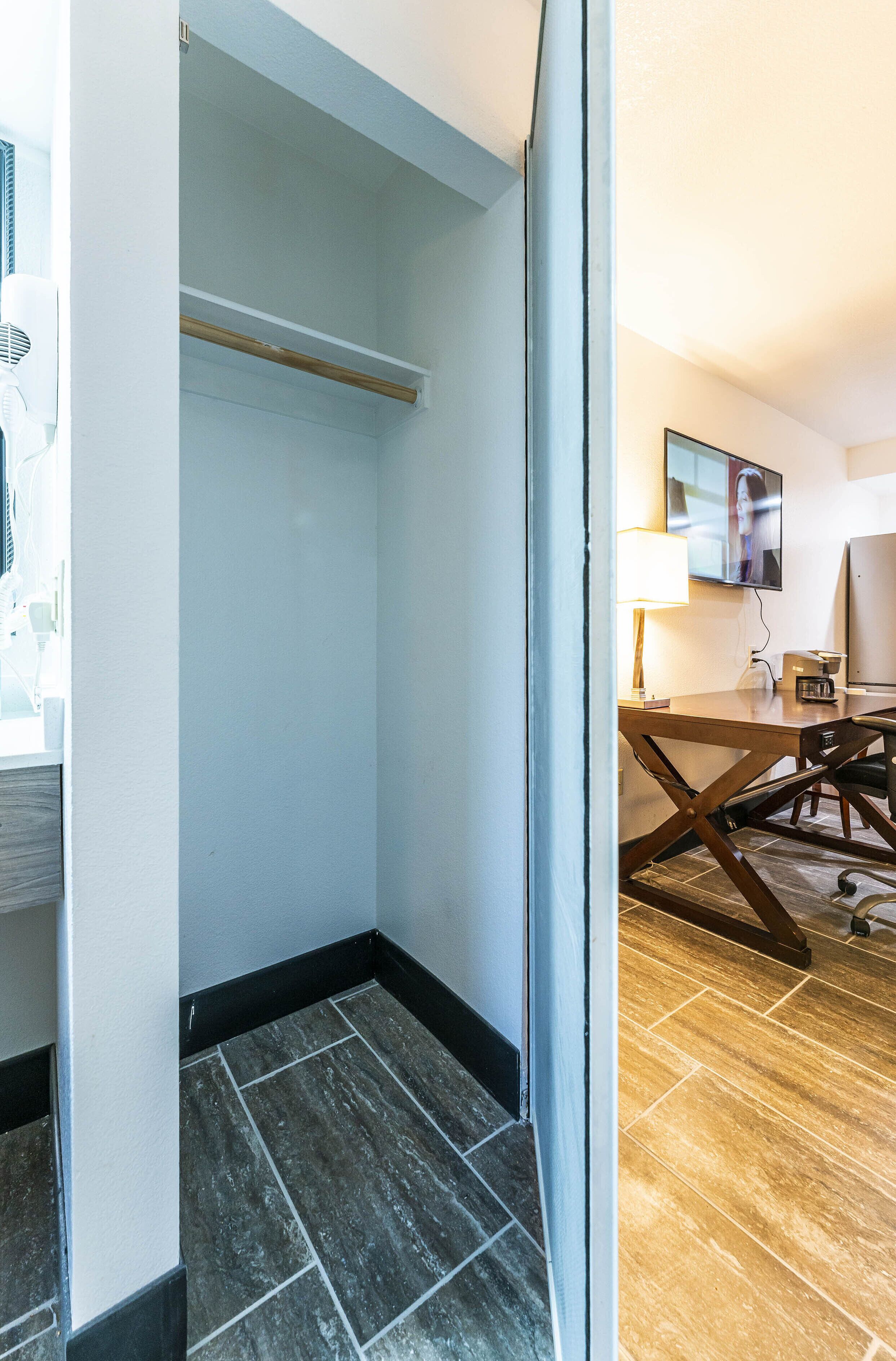 A hotel room with a wooden floor, a desk with a lamp, and a television mounted on the wall.