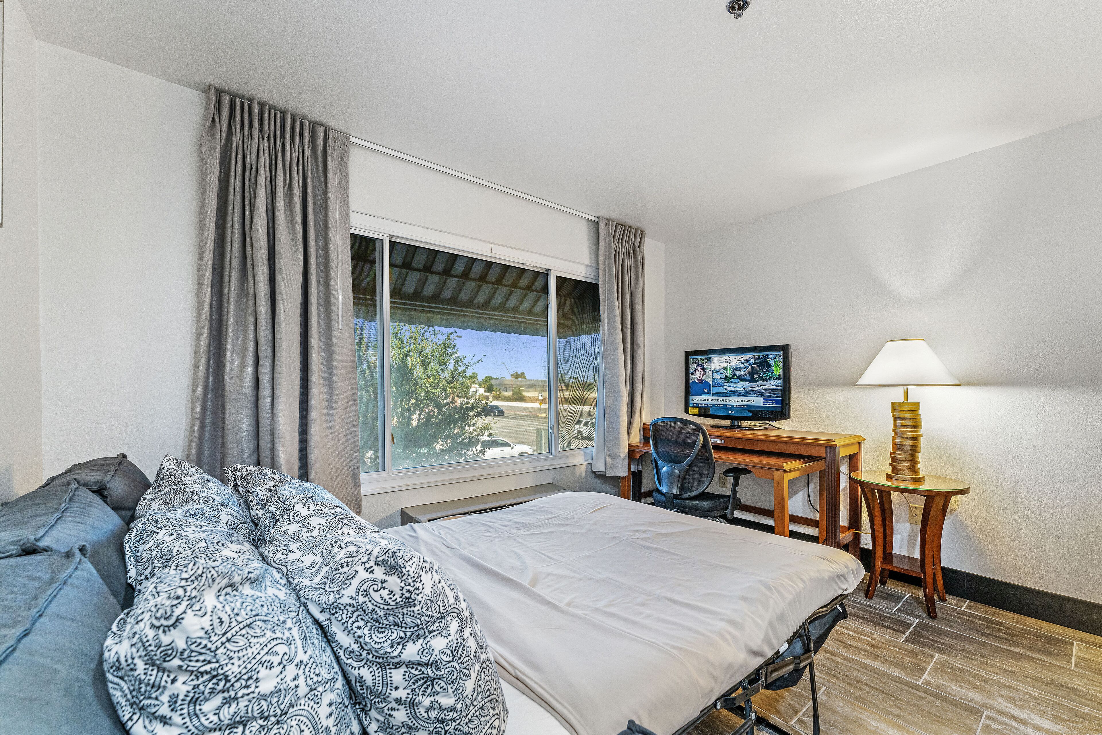A hotel room with a bed, a desk with a chair, a TV, and a lamp.