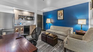 A compact hotel room with a kitchenette, a sofa, a coffee table, and a desk.