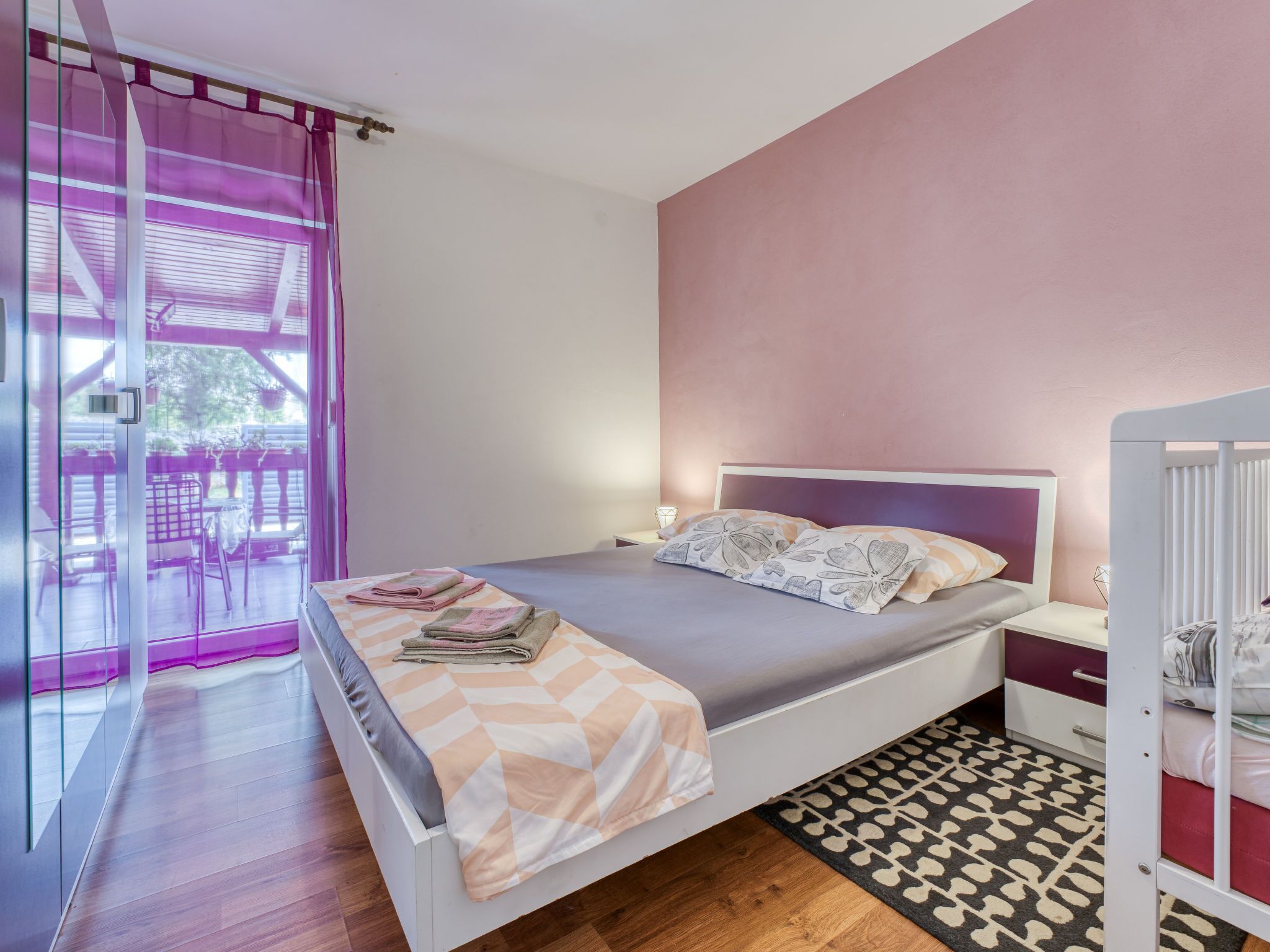 A bedroom with a bed, a bedside table, a nightstand, a window with curtains, and a view of the outside.